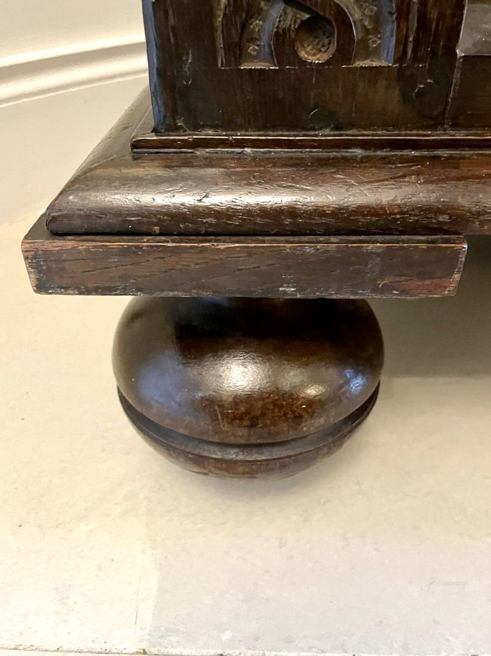 A dark carved oak coffer featuring three arcaded front panels, carved border details, top iron hinges, and turned bun feet. View III