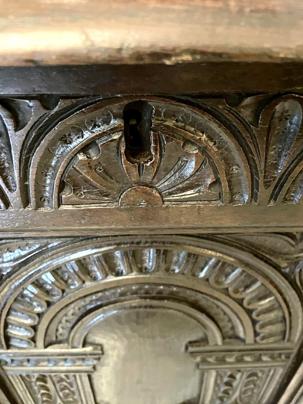A dark carved oak coffer featuring three arcaded front panels, carved border details, top iron hinges, and turned bun feet. View IV
