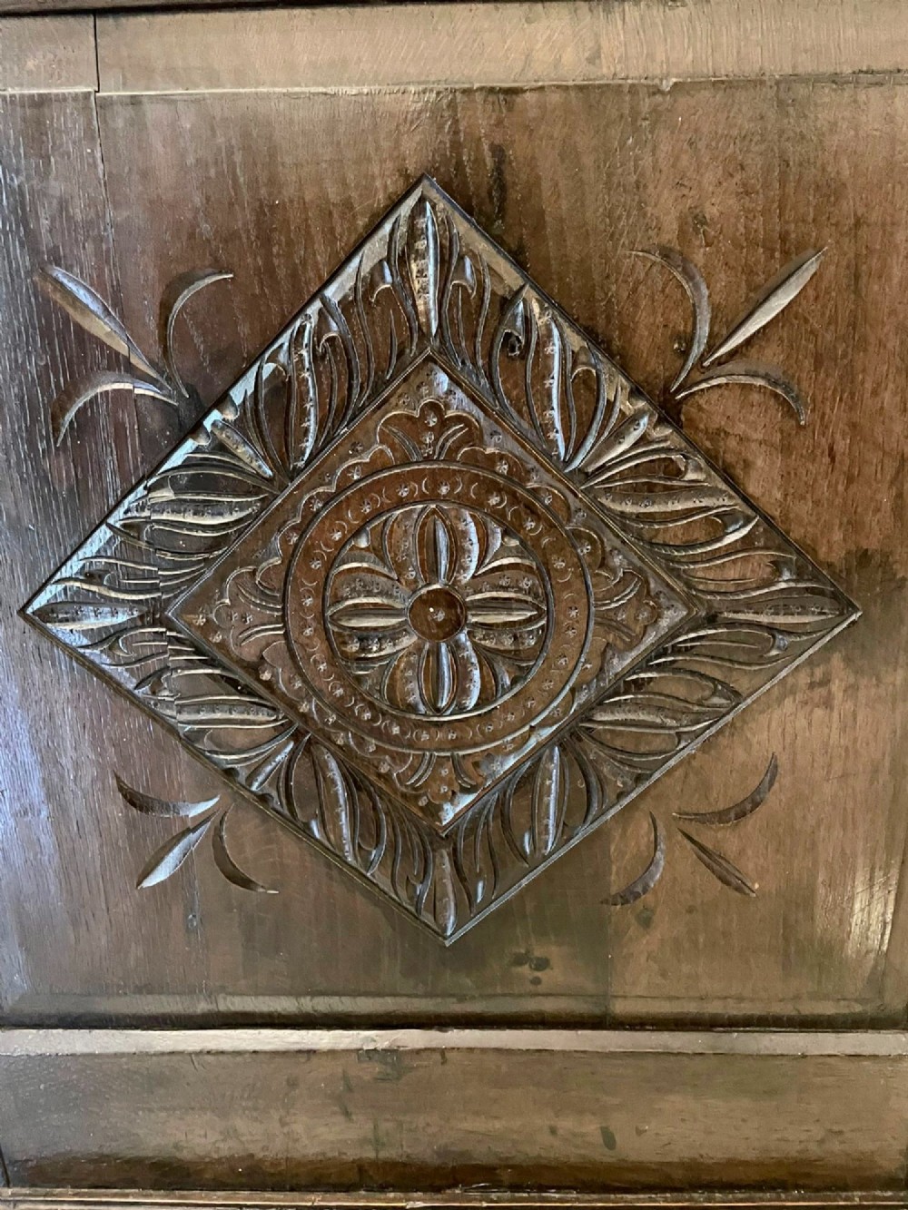 A dark carved oak coffer featuring three arcaded front panels, carved border details, top iron hinges, and turned bun feet. View VI