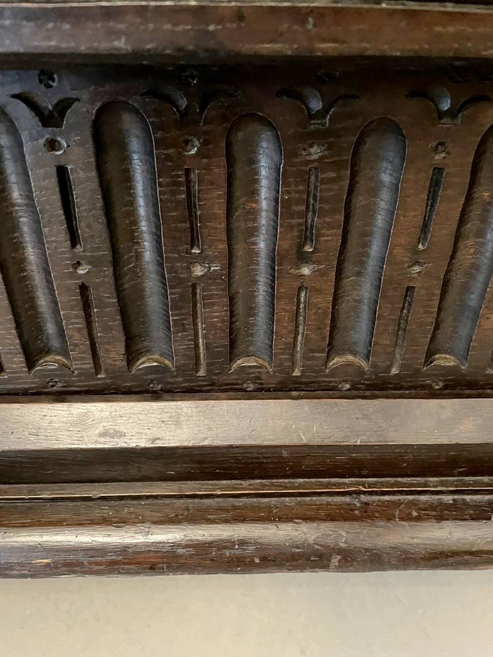 A dark carved oak coffer featuring three arcaded front panels, carved border details, top iron hinges, and turned bun feet. View VII