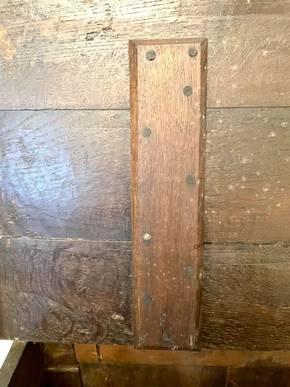 A dark carved oak coffer featuring three arcaded front panels, carved border details, top iron hinges, and turned bun feet. View VIII