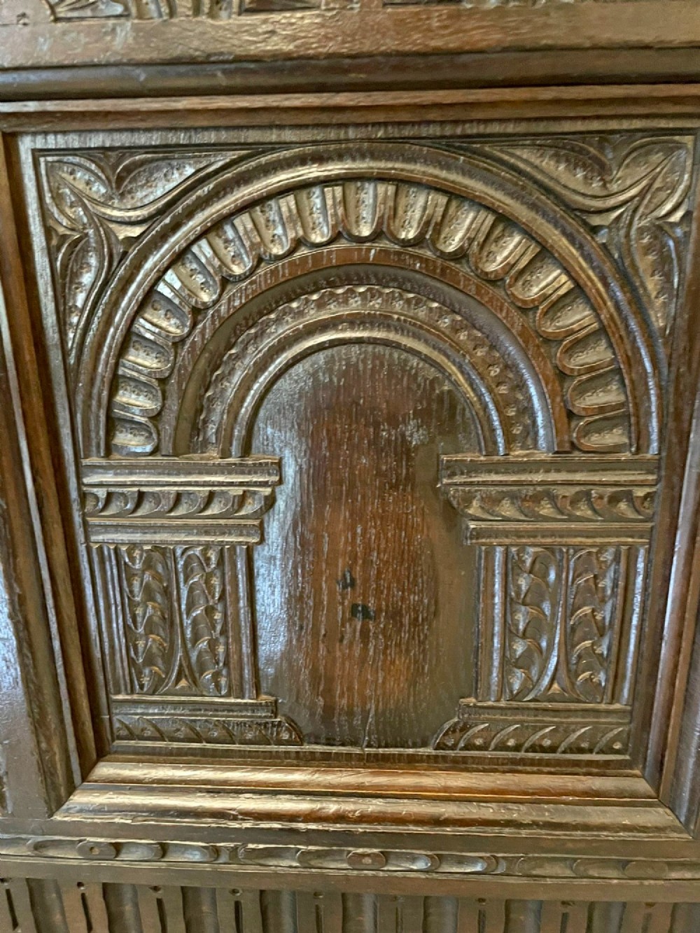 A dark carved oak coffer featuring three arcaded front panels, carved border details, top iron hinges, and turned bun feet. View IX