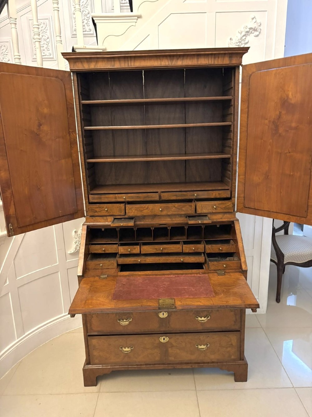 An 18th-century George I figured walnut bureau bookcase featuring two mirrored upper cabinet doors, a slant-front writing desk, and three lower drawers on bracket feet. View V