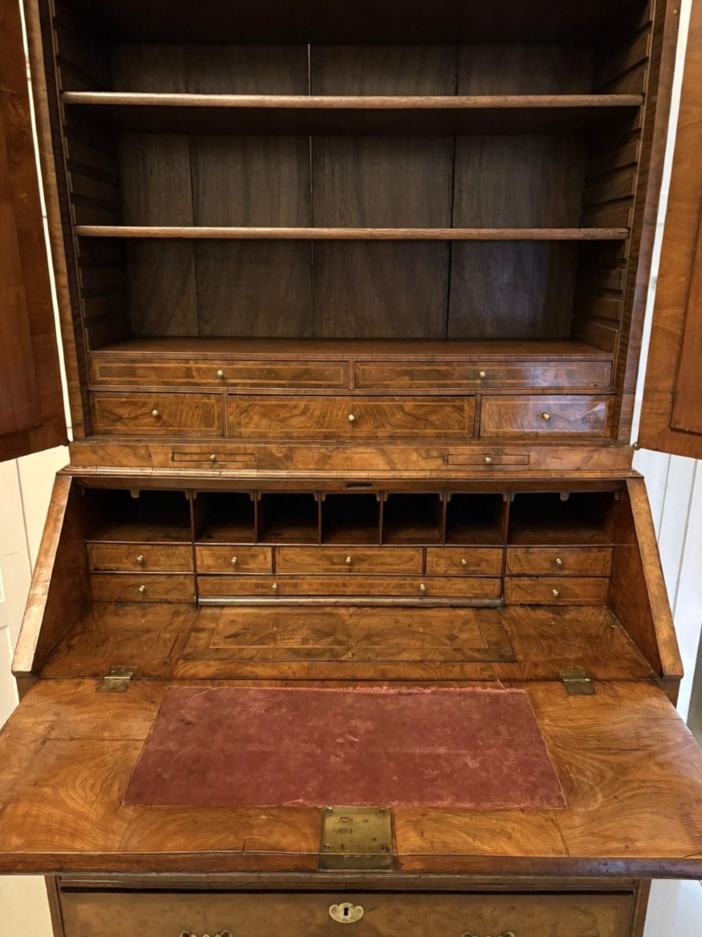 An 18th-century George I figured walnut bureau bookcase featuring two mirrored upper cabinet doors, a slant-front writing desk, and three lower drawers on bracket feet. View X