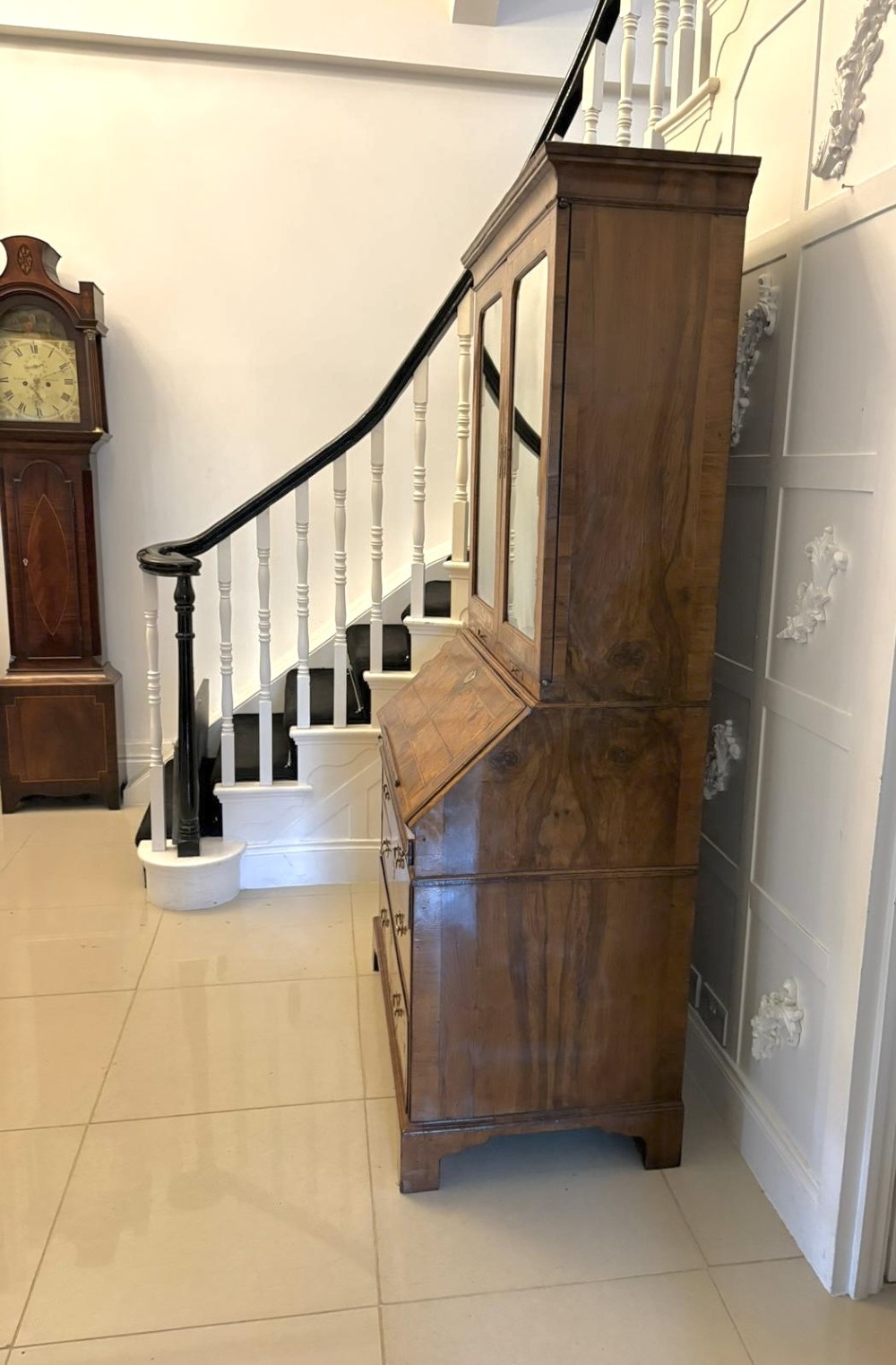 An 18th-century George I figured walnut bureau bookcase featuring two mirrored upper cabinet doors, a slant-front writing desk, and three lower drawers on bracket feet. View XII