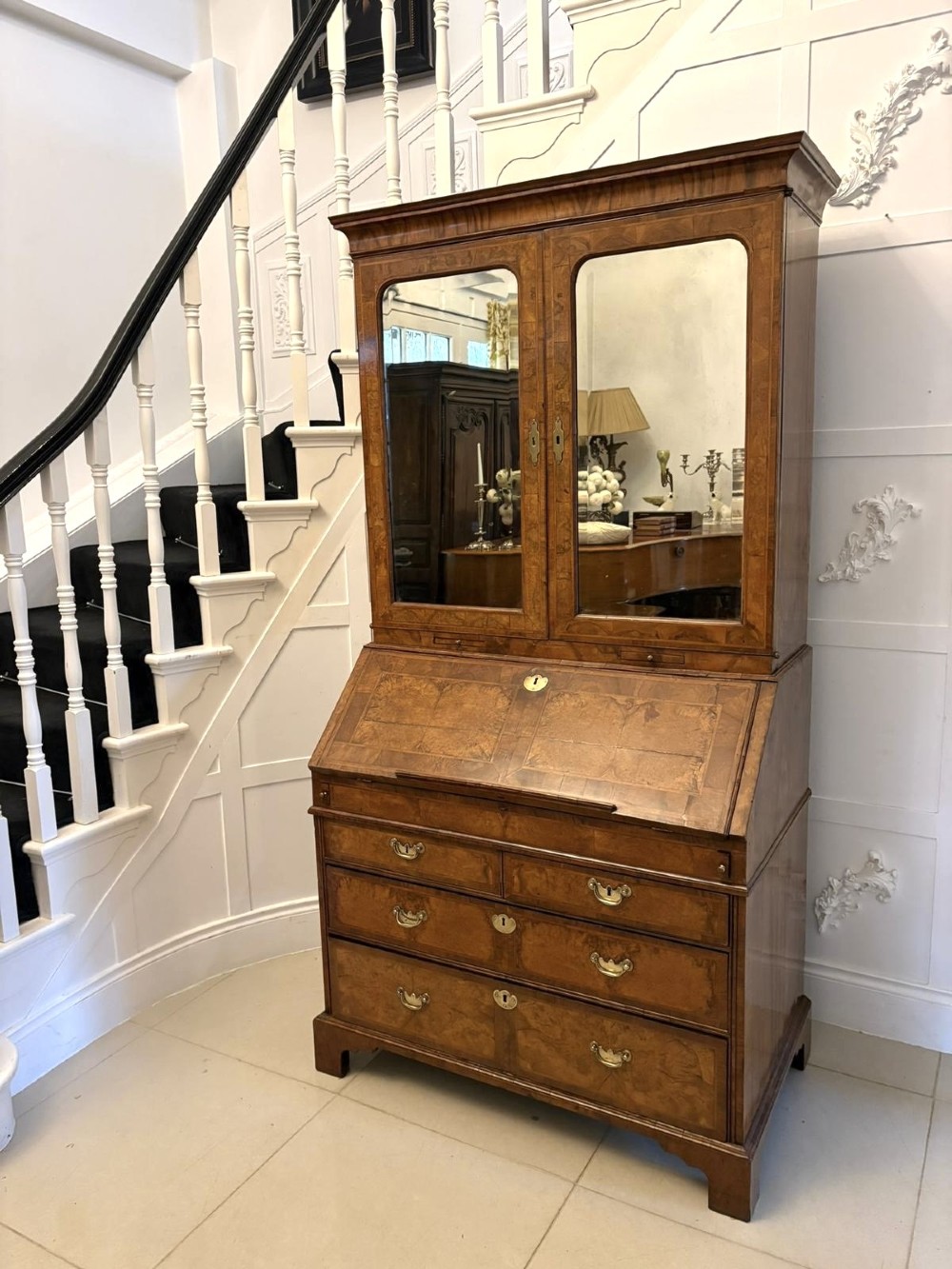 An 18th-century George I figured walnut bureau bookcase featuring two mirrored upper cabinet doors, a slant-front writing desk, and three lower drawers on bracket feet. View XV