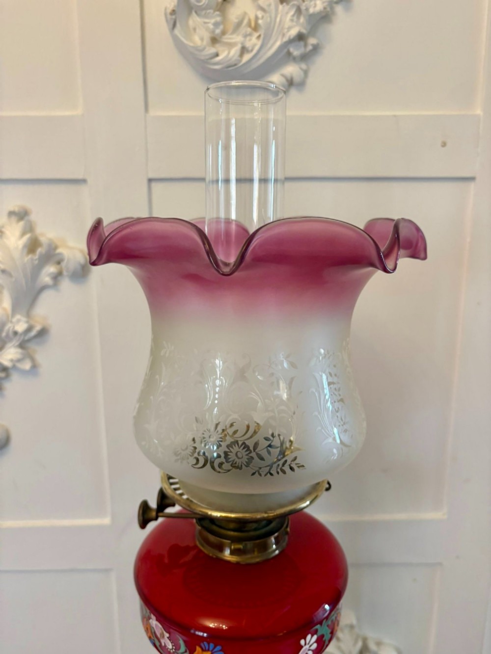 An antique Victorian oil lamp featuring a stepped square brass base, a fluted Corinthian column stem, an enamel-painted red glass font, and an etched cranberry glass frilled shade. View V
