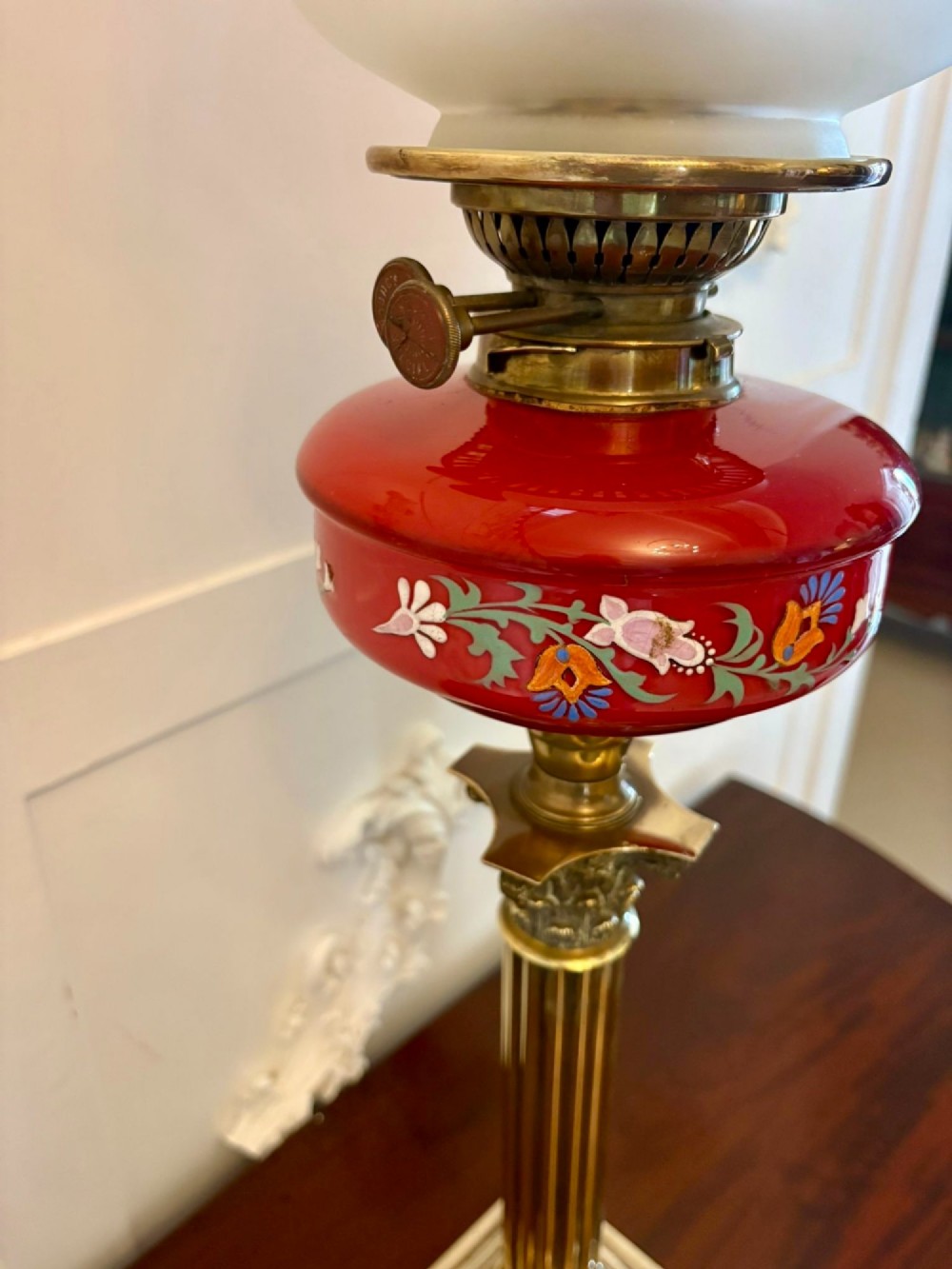 An antique Victorian oil lamp featuring a stepped square brass base, a fluted Corinthian column stem, an enamel-painted red glass font, and an etched cranberry glass frilled shade. View VII