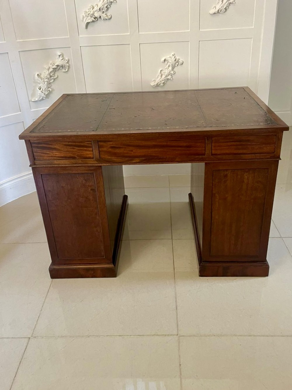A Victorian mahogany freestanding kneehole desk featuring a leather writing insert, multiple drawers with brass handles, and side brass carrying handles. View IV