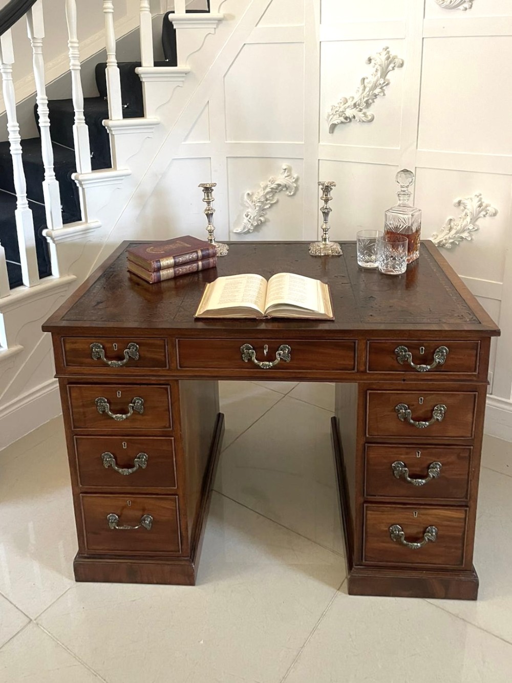 A Victorian mahogany freestanding kneehole desk featuring a leather writing insert, multiple drawers with brass handles, and side brass carrying handles. View V
