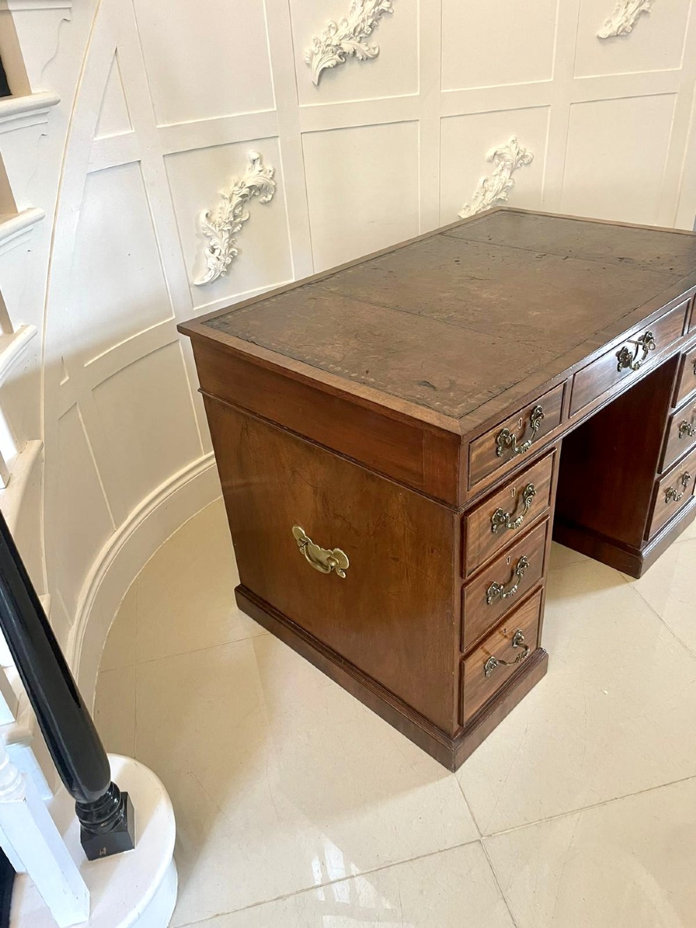 A Victorian mahogany freestanding kneehole desk featuring a leather writing insert, multiple drawers with brass handles, and side brass carrying handles. View VI