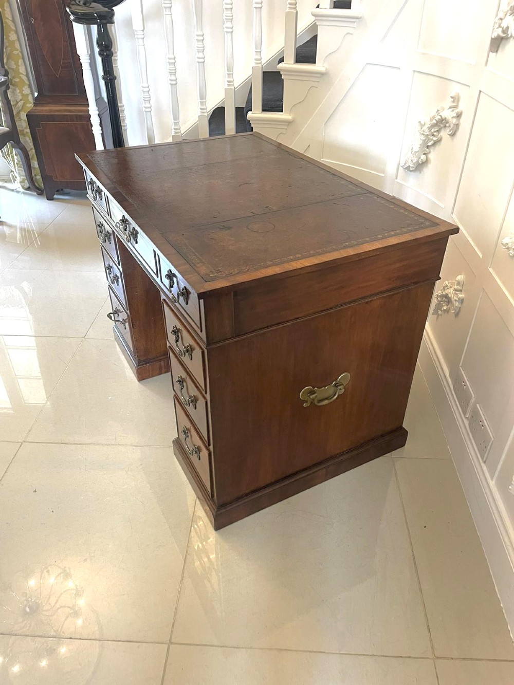 A Victorian mahogany freestanding kneehole desk featuring a leather writing insert, multiple drawers with brass handles, and side brass carrying handles. View VII