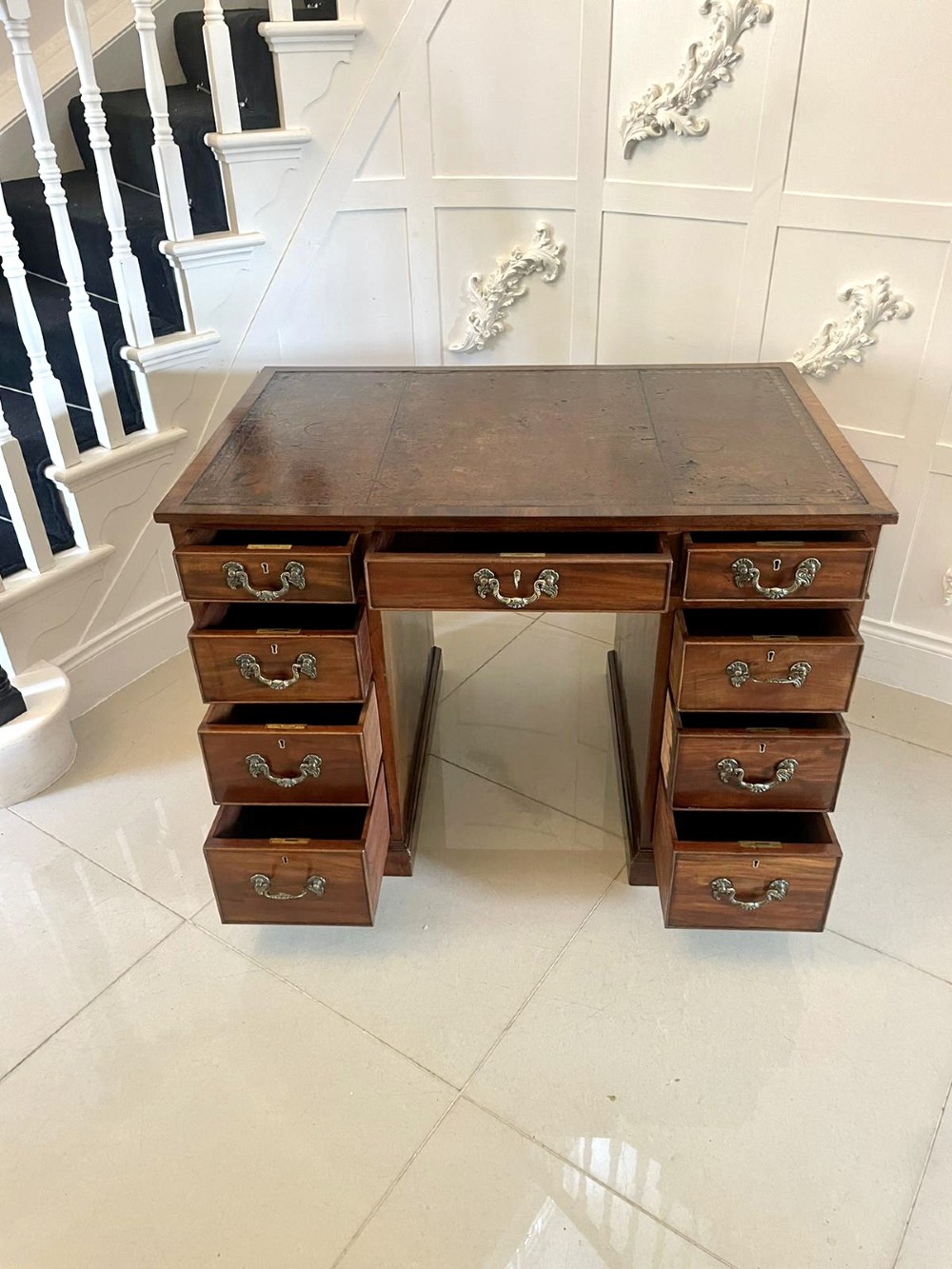 A Victorian mahogany freestanding kneehole desk featuring a leather writing insert, multiple drawers with brass handles, and side brass carrying handles. View VIII