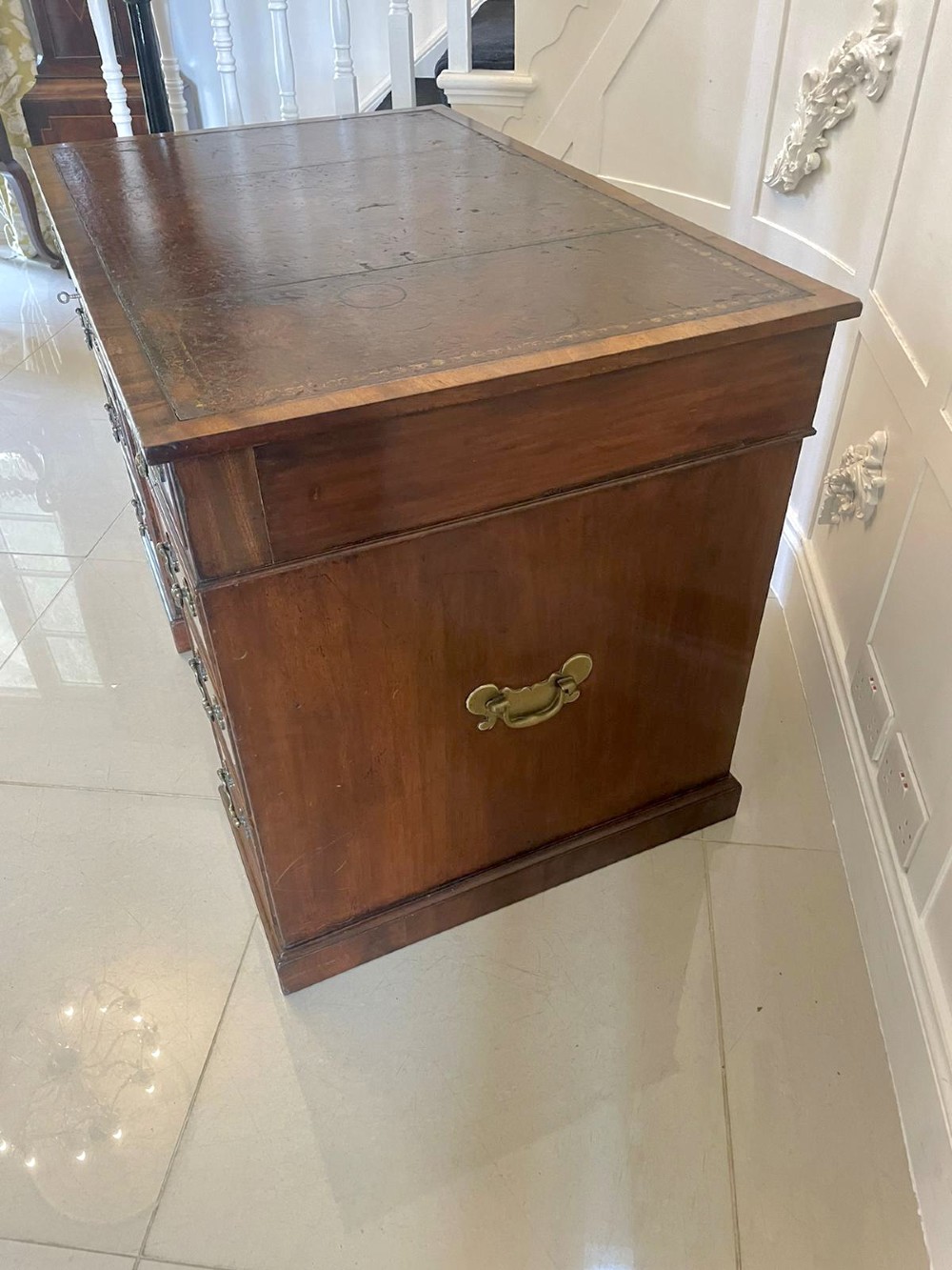 A Victorian mahogany freestanding kneehole desk featuring a leather writing insert, multiple drawers with brass handles, and side brass carrying handles. View IX