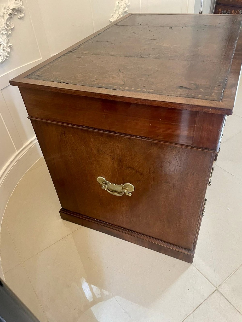 A Victorian mahogany freestanding kneehole desk featuring a leather writing insert, multiple drawers with brass handles, and side brass carrying handles. View X