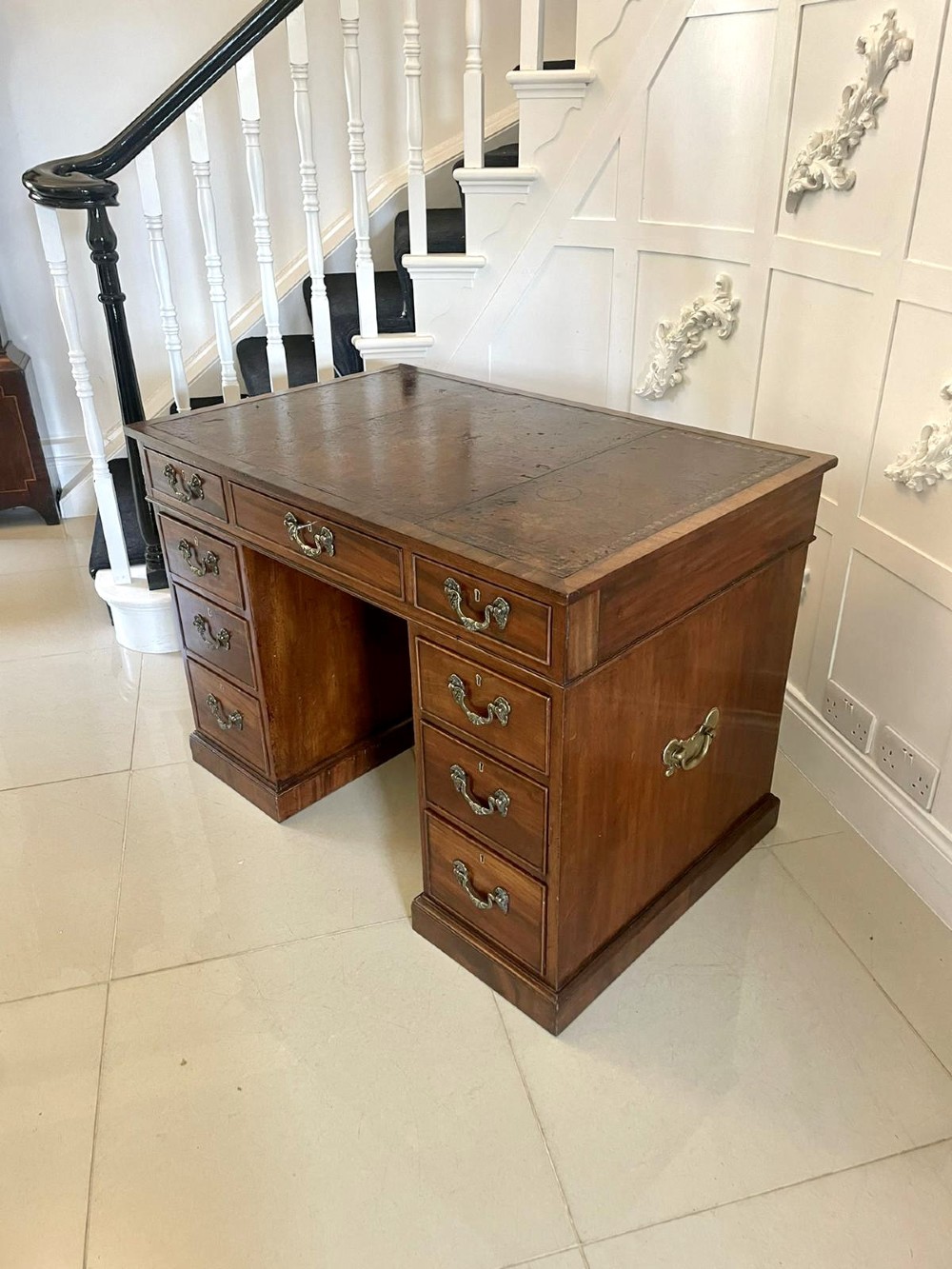 A Victorian mahogany freestanding kneehole desk featuring a leather writing insert, multiple drawers with brass handles, and side brass carrying handles. View XII