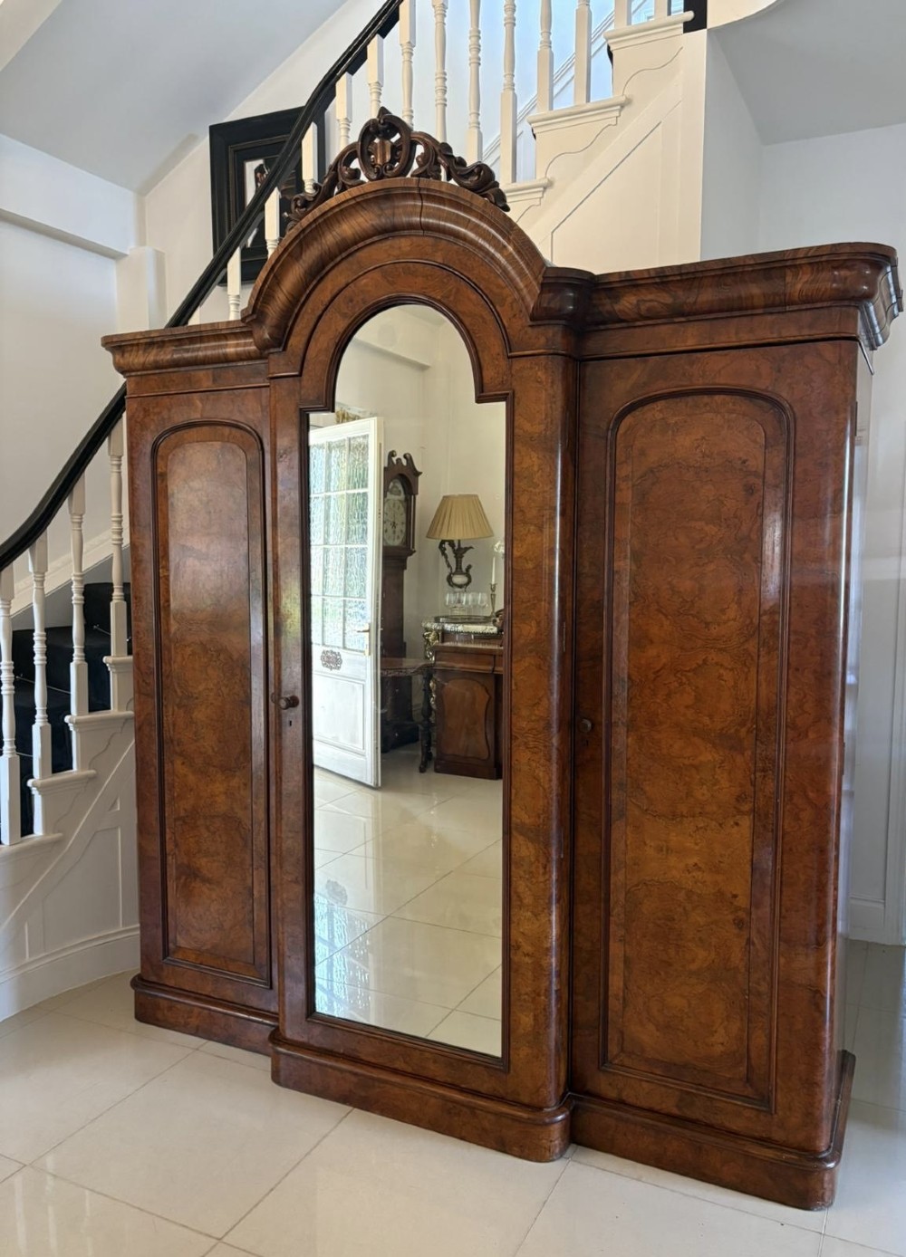 An antique Victorian burr walnut three-door wardrobe featuring an arched central mirrored door crowned with a carved crest, flanked by two burr walnut panelled doors. View V