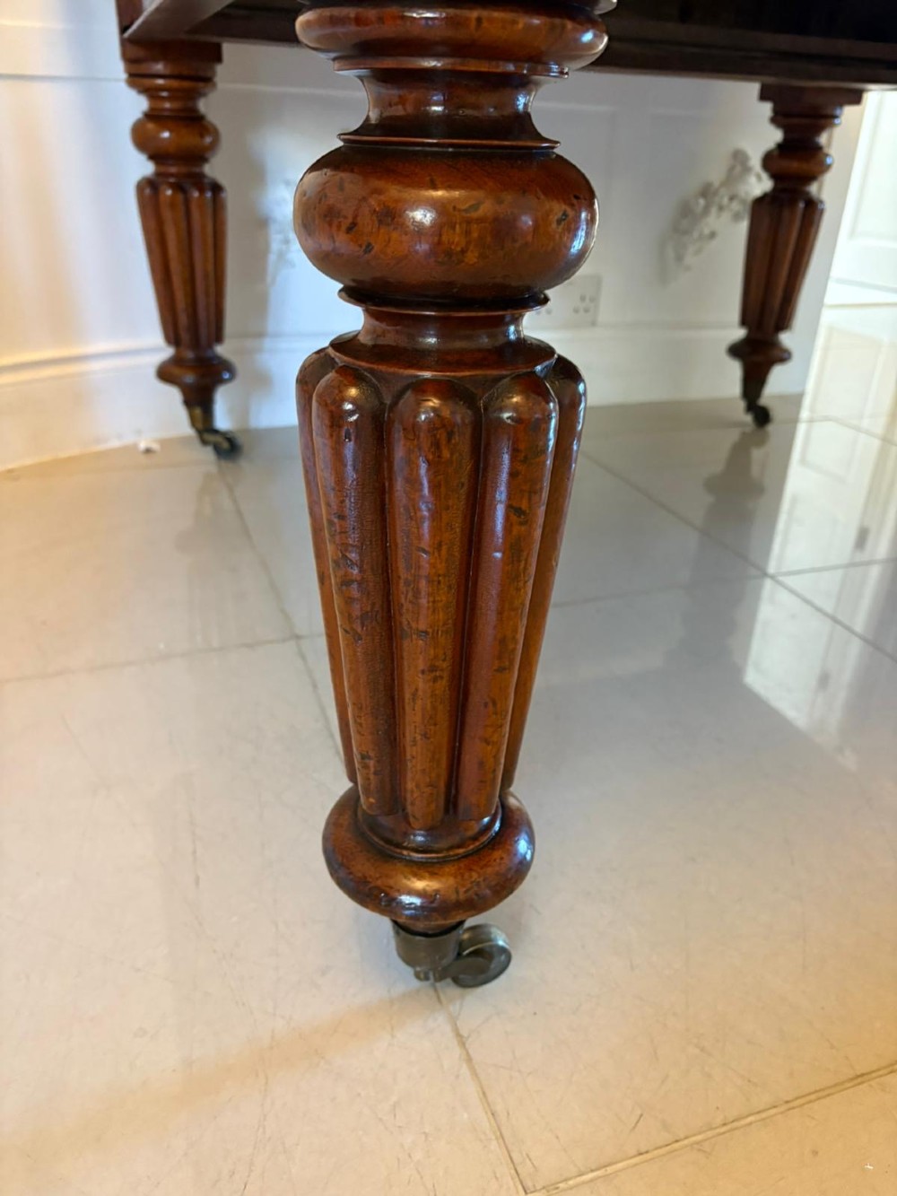 A large Victorian mahogany extending dining table with a polished surface, moulded rim, additional leaves, and turned fluted legs on brass castors. View IV
