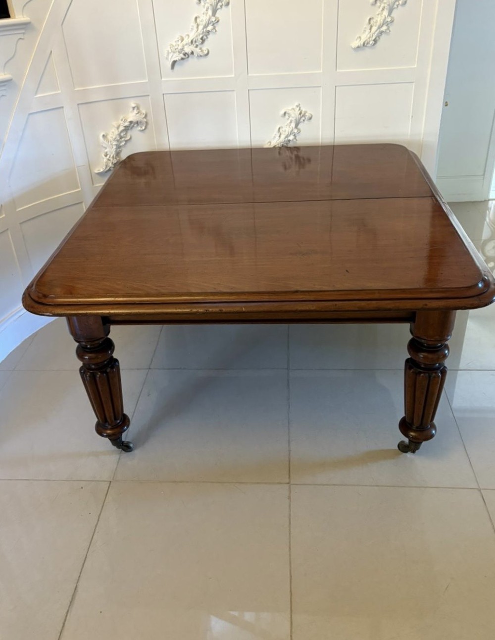 A large Victorian mahogany extending dining table with a polished surface, moulded rim, additional leaves, and turned fluted legs on brass castors. View V