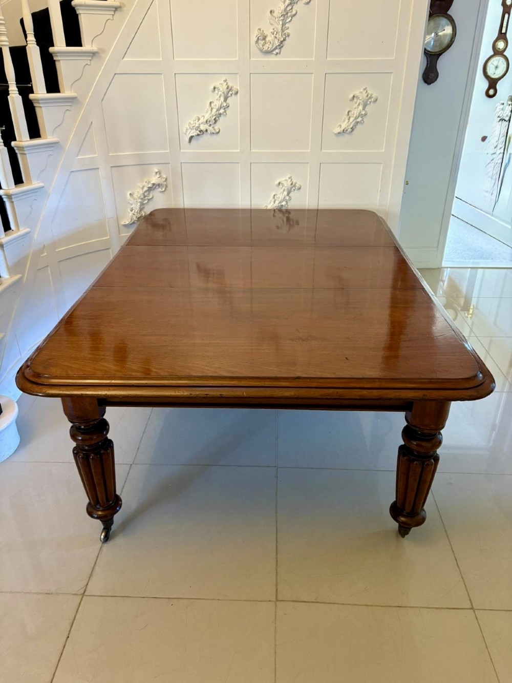 A large Victorian mahogany extending dining table with a polished surface, moulded rim, additional leaves, and turned fluted legs on brass castors. View VII