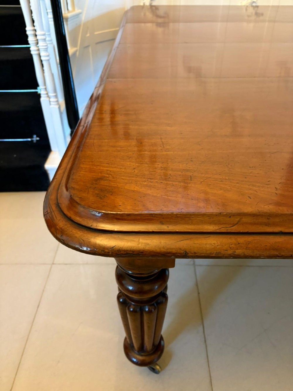 A large Victorian mahogany extending dining table with a polished surface, moulded rim, additional leaves, and turned fluted legs on brass castors. View XI