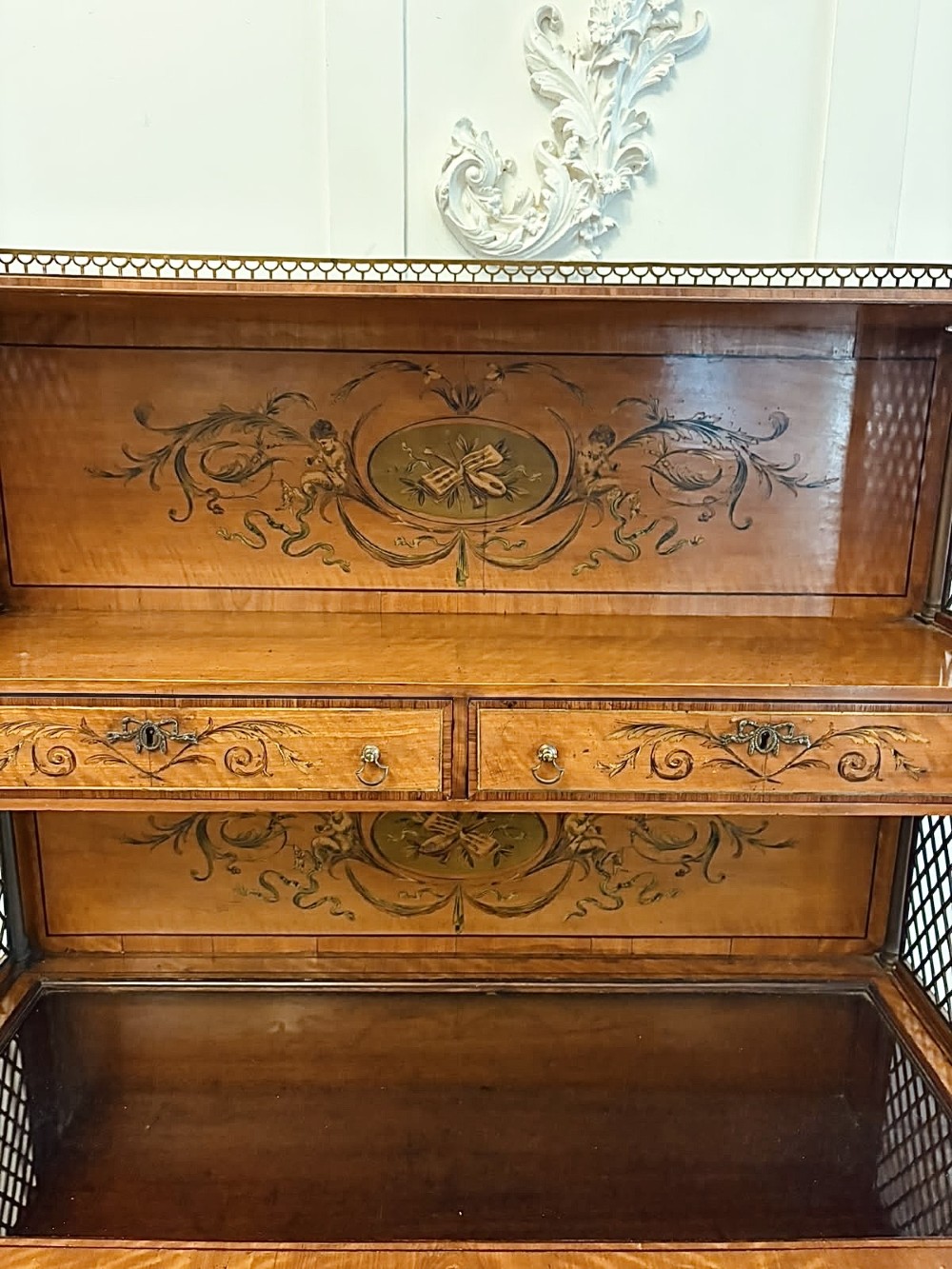 A Georgian Sheraton style satinwood display cabinet featuring upper open shelves with brass grilles and marquetry panels, positioned above a lower glazed twin-door cabinet with oval astragal bars. View IX