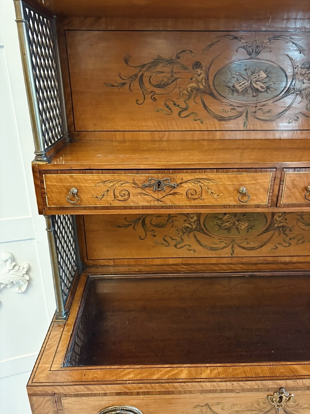 A Georgian Sheraton style satinwood display cabinet featuring upper open shelves with brass grilles and marquetry panels, positioned above a lower glazed twin-door cabinet with oval astragal bars. View X