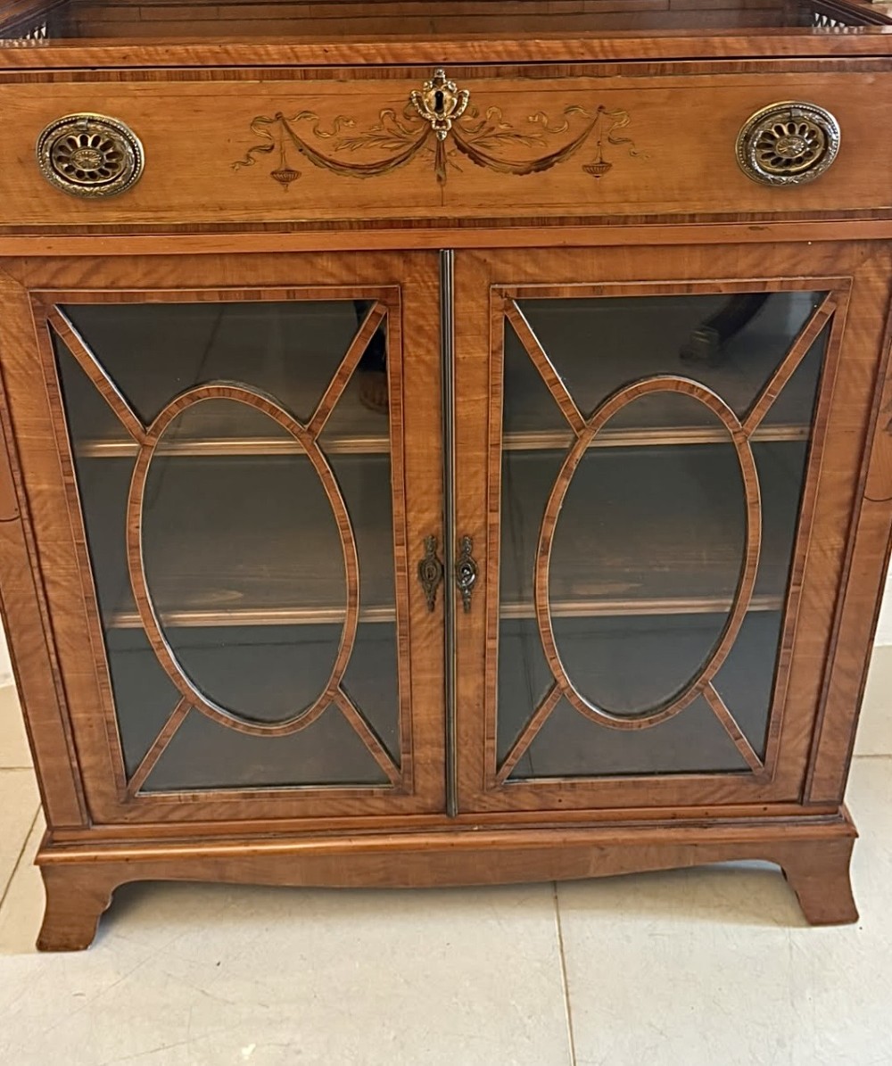 A Georgian Sheraton style satinwood display cabinet featuring upper open shelves with brass grilles and marquetry panels, positioned above a lower glazed twin-door cabinet with oval astragal bars. View XII