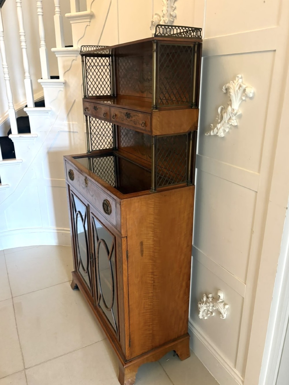 A Georgian Sheraton style satinwood display cabinet featuring upper open shelves with brass grilles and marquetry panels, positioned above a lower glazed twin-door cabinet with oval astragal bars. View XIII
