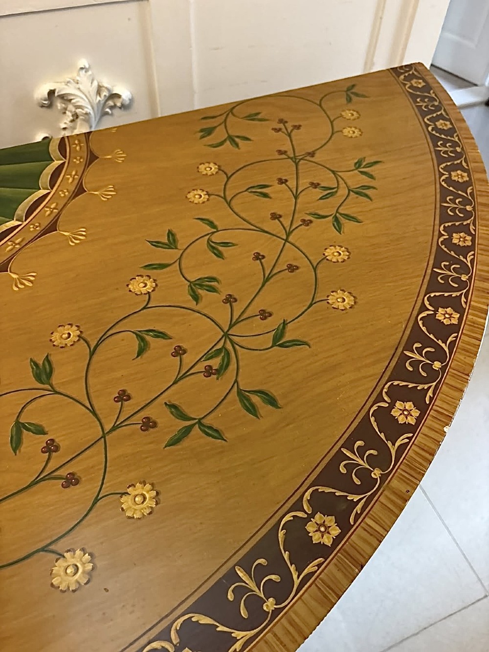 A semicircular satinwood demi-lune cabinet featuring hand-painted neoclassical leaf swags, a central figural medallion, and short tapered feet. View VI