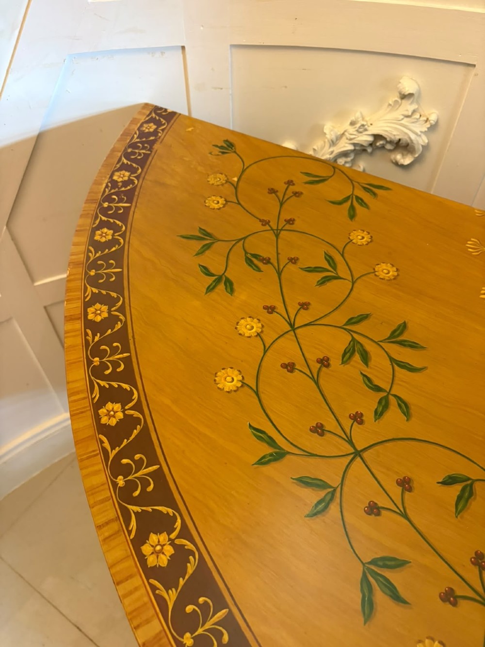 A semicircular satinwood demi-lune cabinet featuring hand-painted neoclassical leaf swags, a central figural medallion, and short tapered feet. View VII
