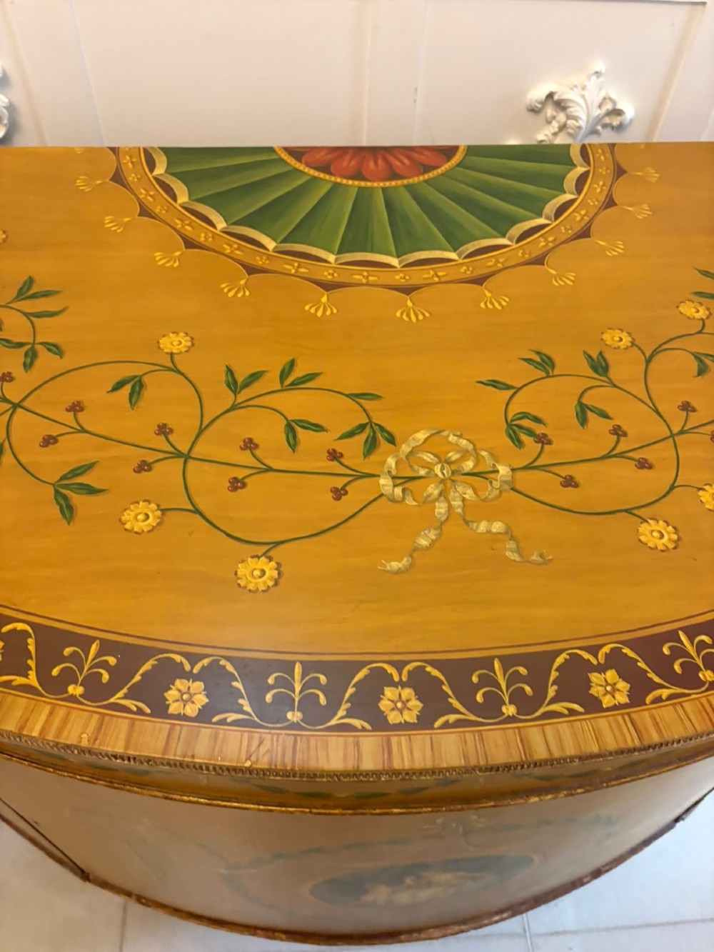 A semicircular satinwood demi-lune cabinet featuring hand-painted neoclassical leaf swags, a central figural medallion, and short tapered feet. View IX