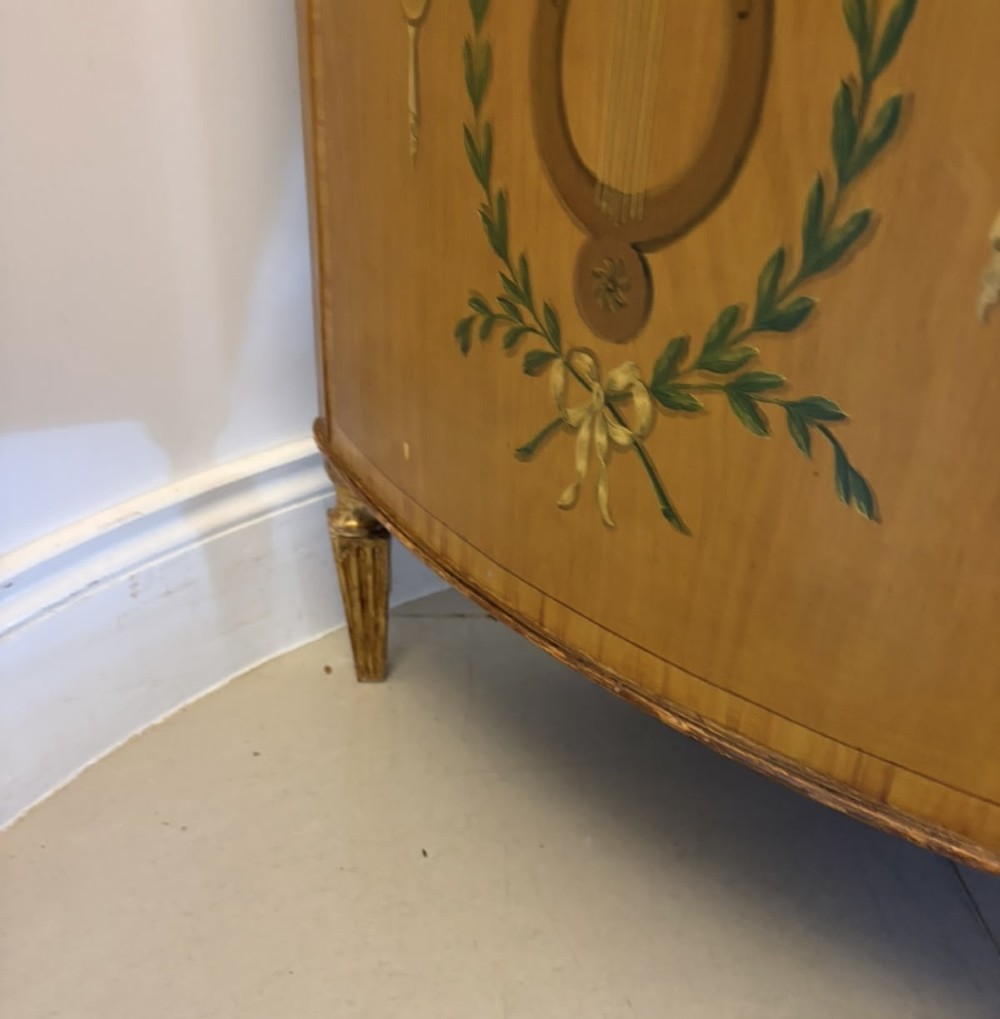 A semicircular satinwood demi-lune cabinet featuring hand-painted neoclassical leaf swags, a central figural medallion, and short tapered feet. View XI