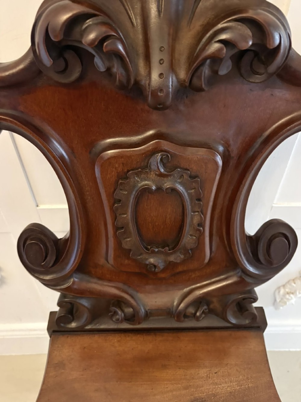 A pair of Victorian carved mahogany hall chairs with shaped timber seats, scrolled cartouche backrests, and carved cabriole legs. View V