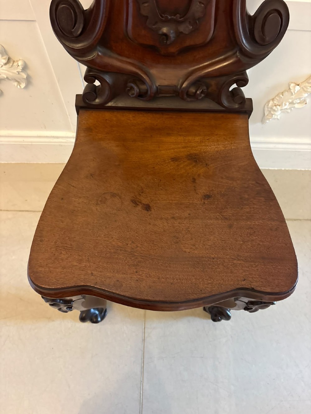 A pair of Victorian carved mahogany hall chairs with shaped timber seats, scrolled cartouche backrests, and carved cabriole legs. View VI