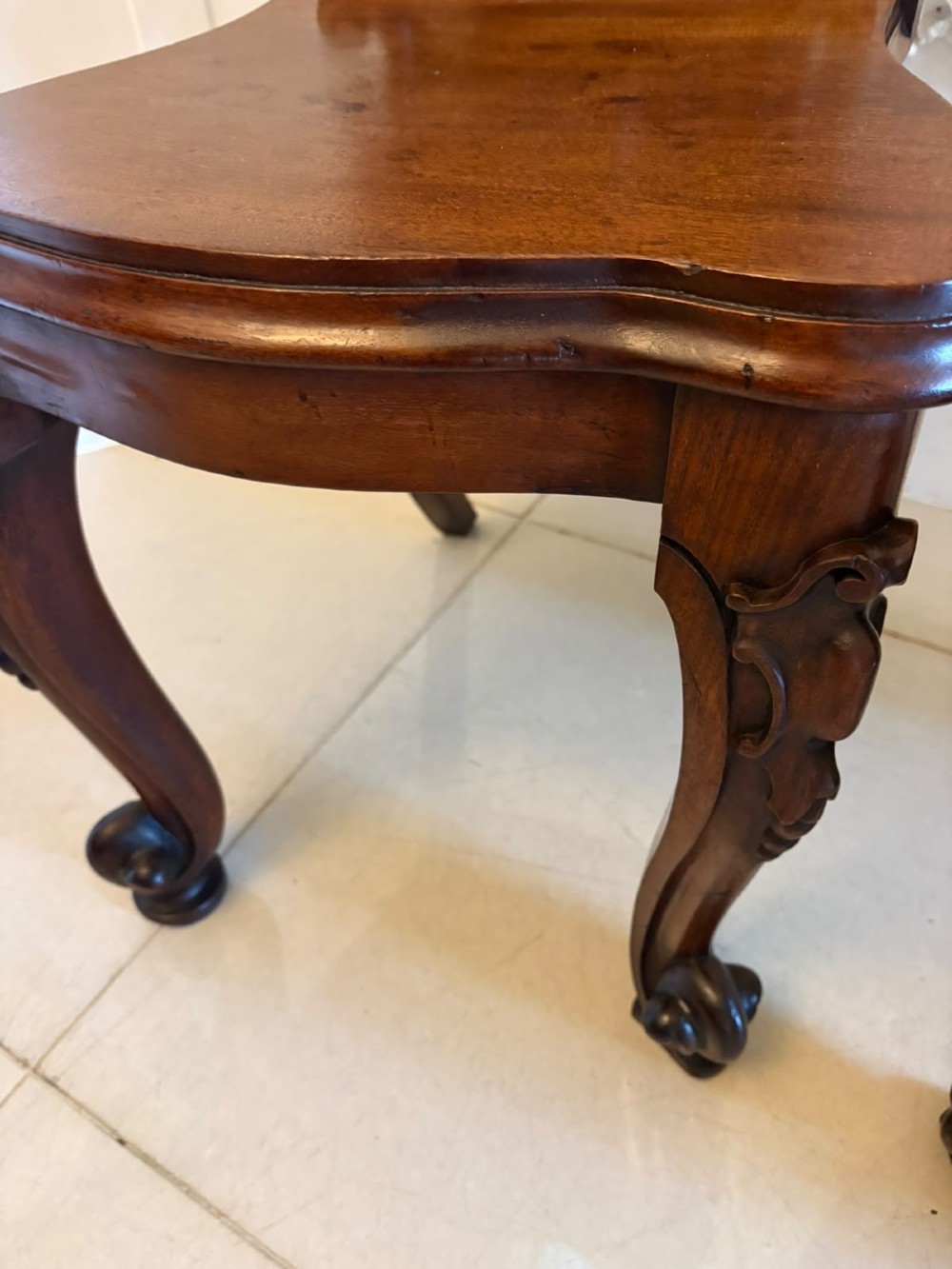 A pair of Victorian carved mahogany hall chairs with shaped timber seats, scrolled cartouche backrests, and carved cabriole legs. View XI