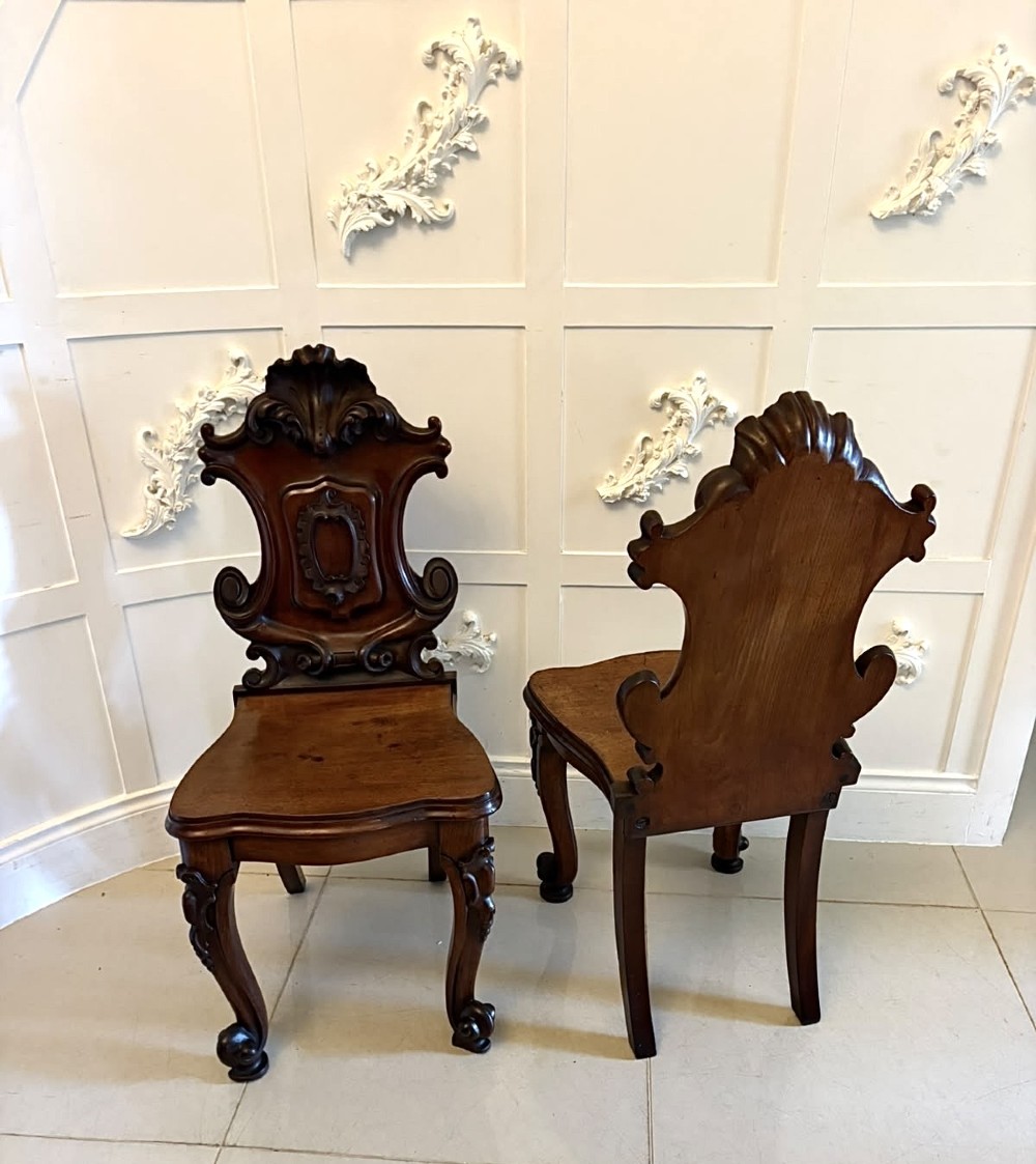 A pair of Victorian carved mahogany hall chairs with shaped timber seats, scrolled cartouche backrests, and carved cabriole legs. View XII
