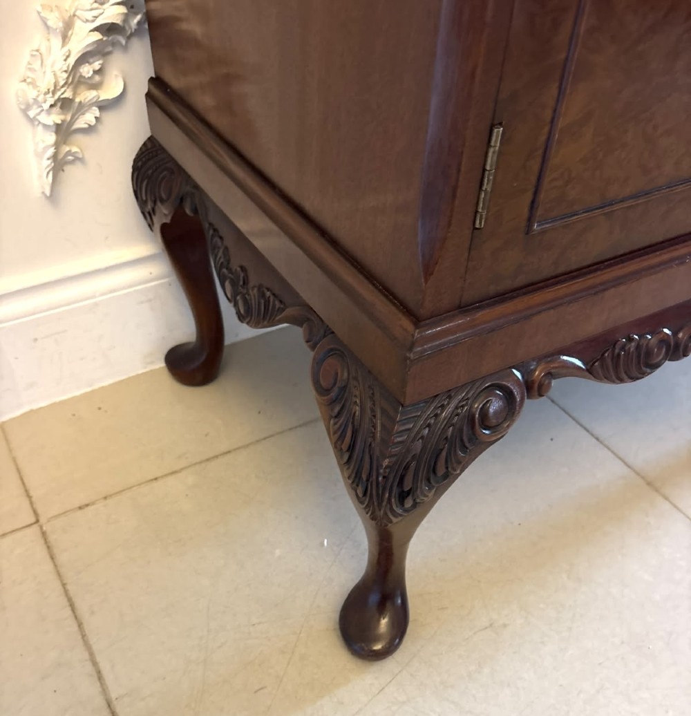An antique burr walnut cocktail cabinet featuring decorative brass hardware, carved scroll cresting, two cupboard sections, and cabriole legs. View IV