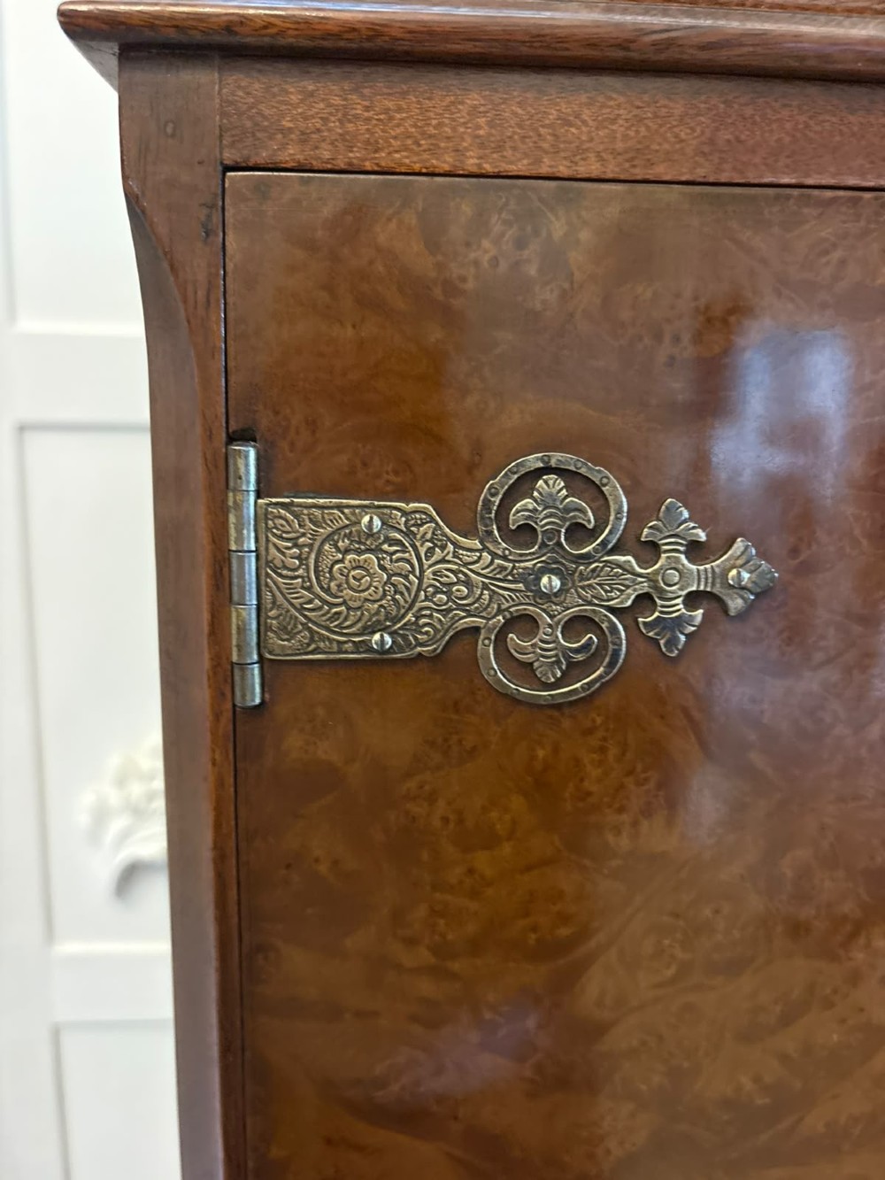 An antique burr walnut cocktail cabinet featuring decorative brass hardware, carved scroll cresting, two cupboard sections, and cabriole legs. View V