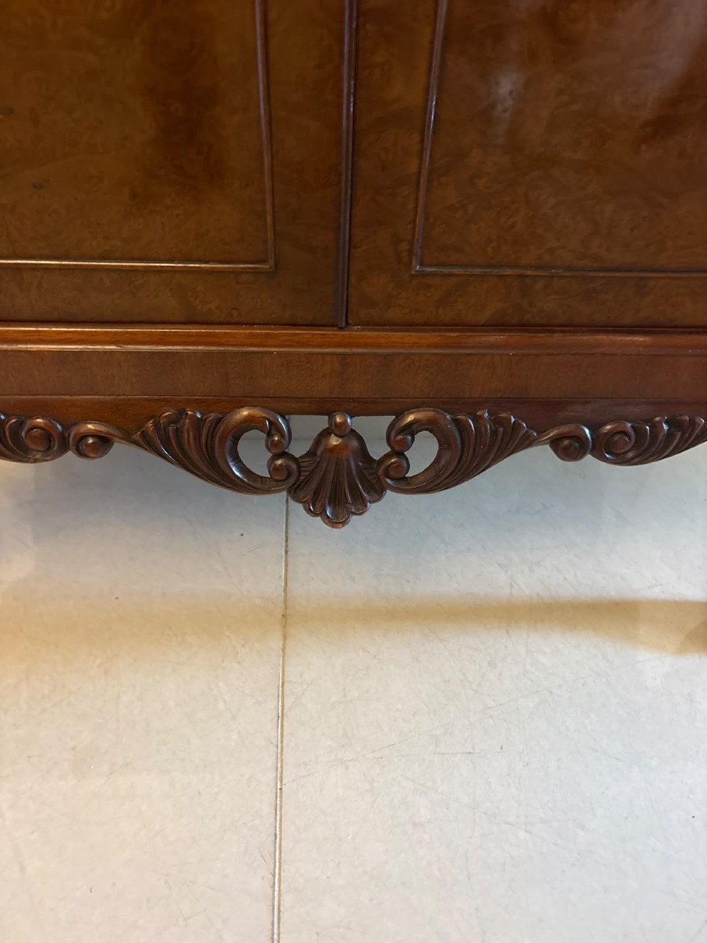 An antique burr walnut cocktail cabinet featuring decorative brass hardware, carved scroll cresting, two cupboard sections, and cabriole legs. View VI