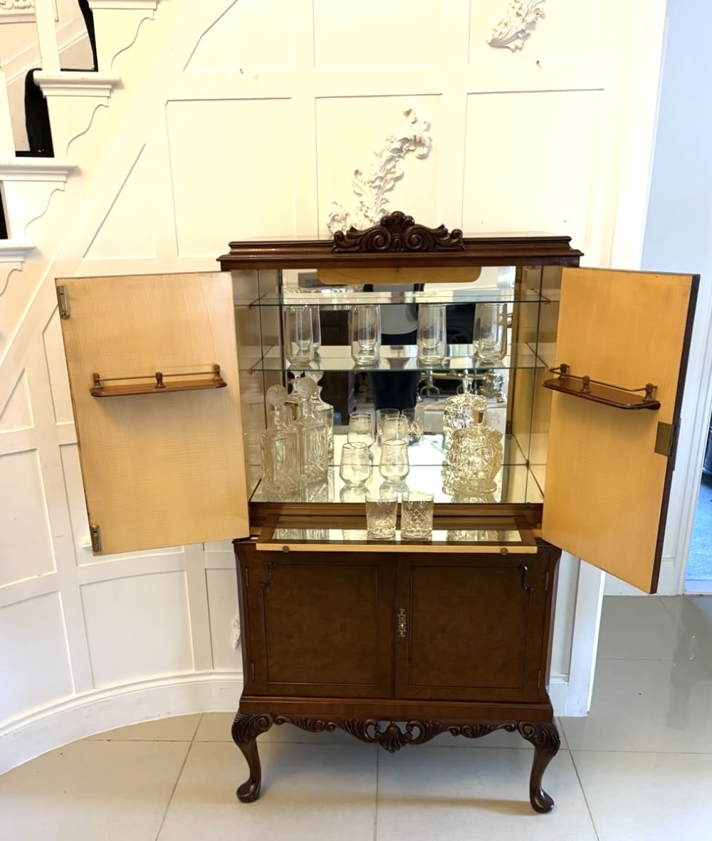 An antique burr walnut cocktail cabinet featuring decorative brass hardware, carved scroll cresting, two cupboard sections, and cabriole legs. View VIII
