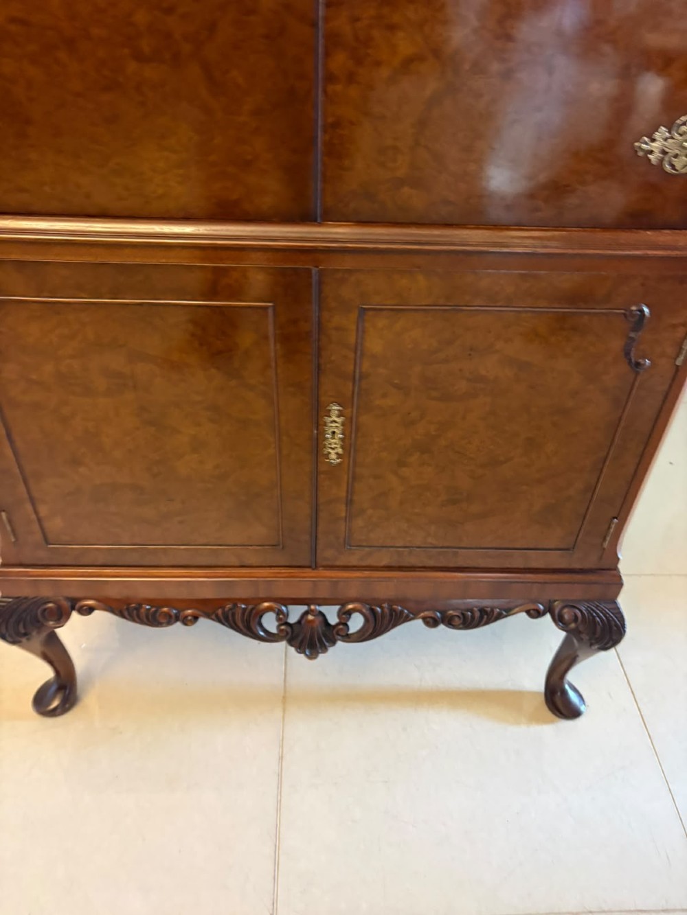 An antique burr walnut cocktail cabinet featuring decorative brass hardware, carved scroll cresting, two cupboard sections, and cabriole legs. View X