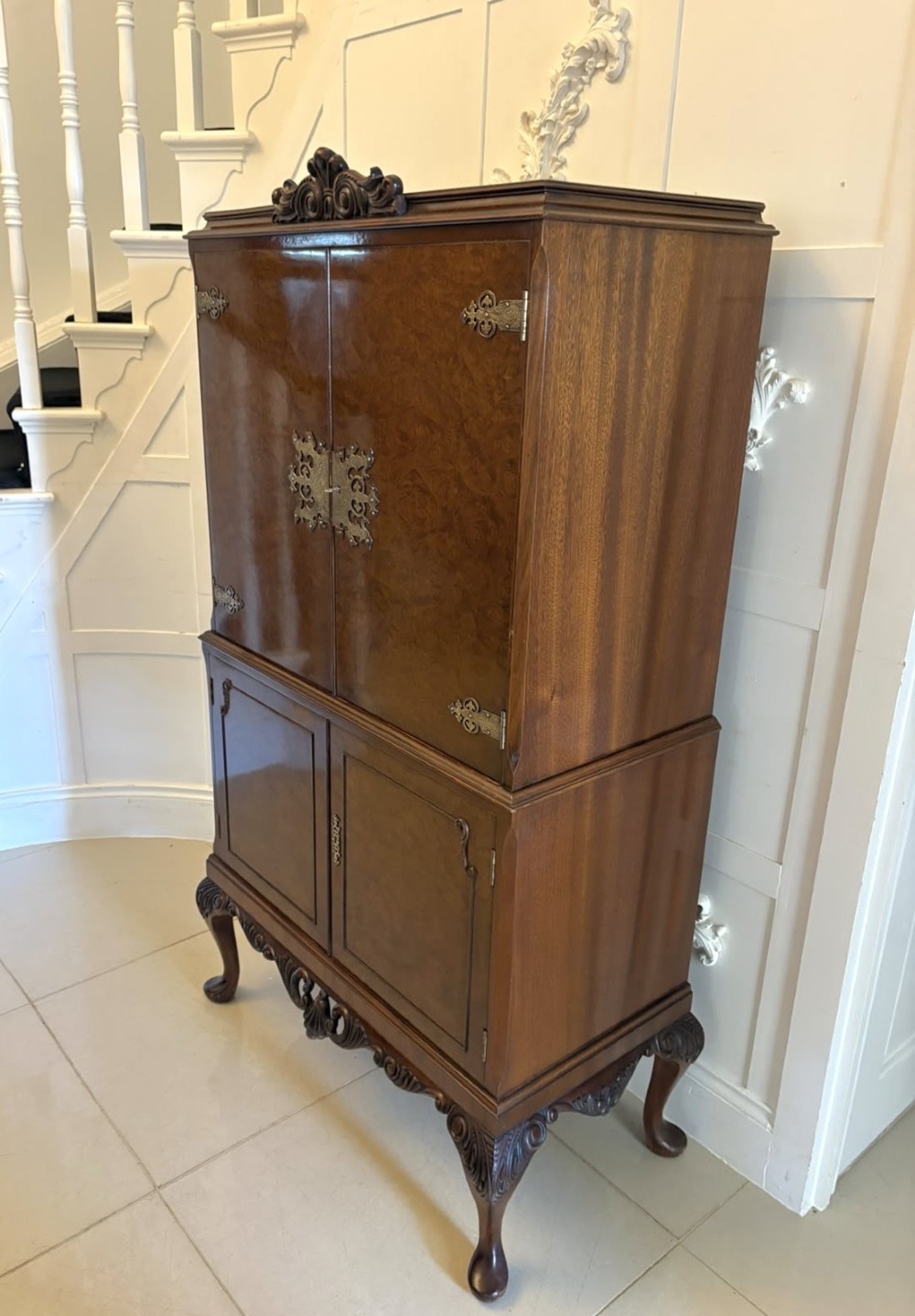 An antique burr walnut cocktail cabinet featuring decorative brass hardware, carved scroll cresting, two cupboard sections, and cabriole legs. View XII