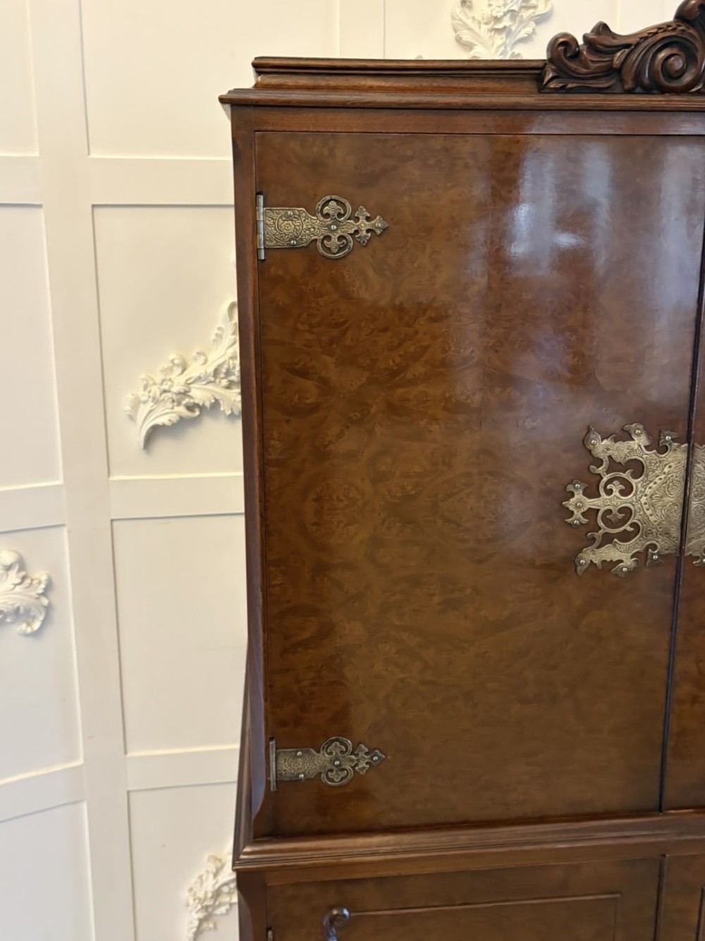 An antique burr walnut cocktail cabinet featuring decorative brass hardware, carved scroll cresting, two cupboard sections, and cabriole legs. View XIV