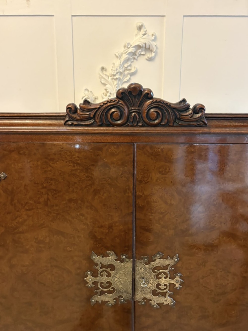 An antique burr walnut cocktail cabinet featuring decorative brass hardware, carved scroll cresting, two cupboard sections, and cabriole legs. View XV