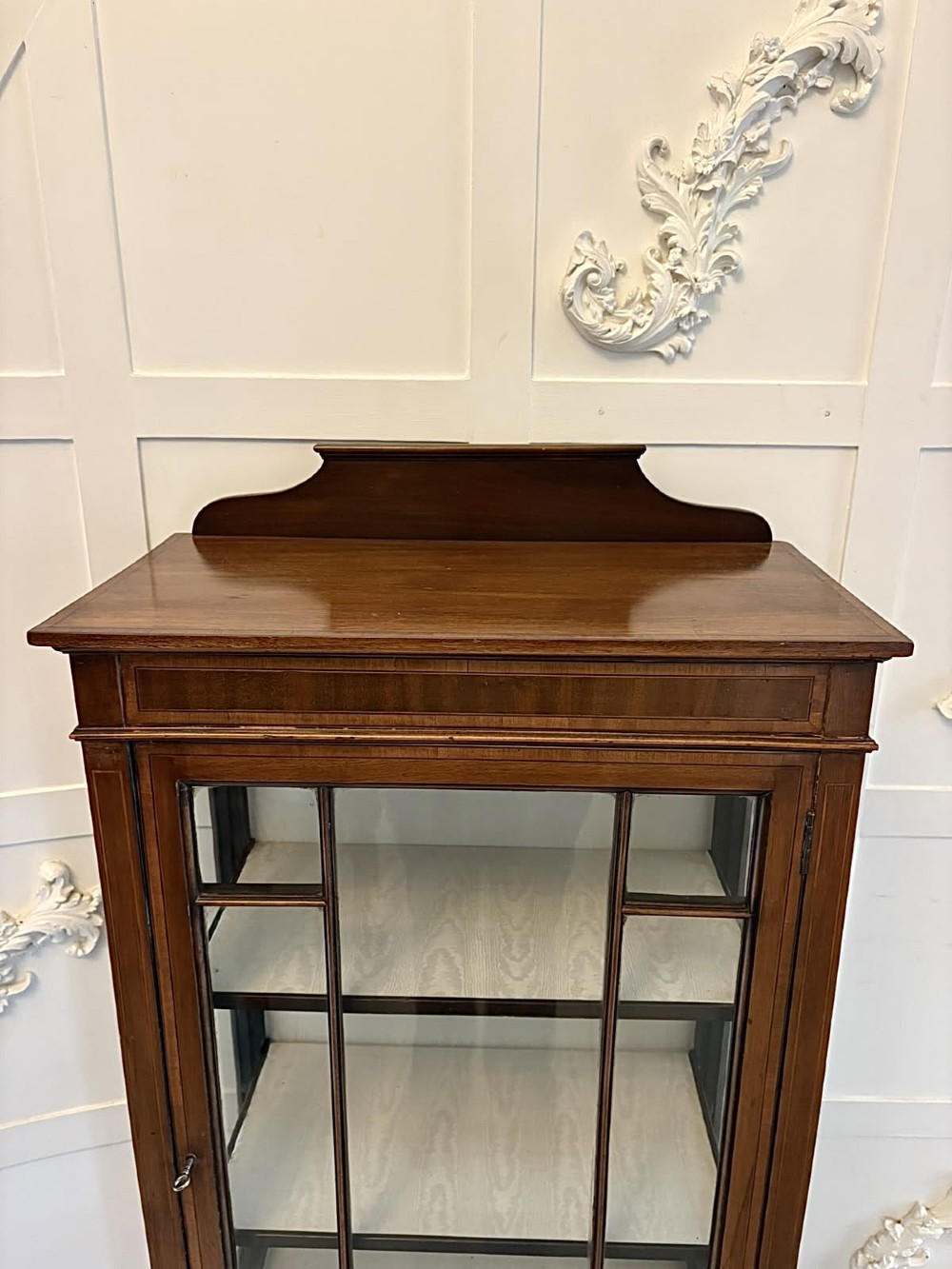 An Edwardian mahogany glazed display cabinet featuring geometric glazing bars, tapered legs, a raised pediment top, and a light-lined interior with three shelves. View VIII