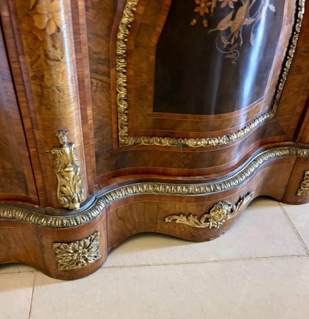 A Victorian serpentine burr walnut credenza featuring detailed floral marquetry inlays, gilt-bronze mounts, a central panelled door, and two curved glazed side doors. View V