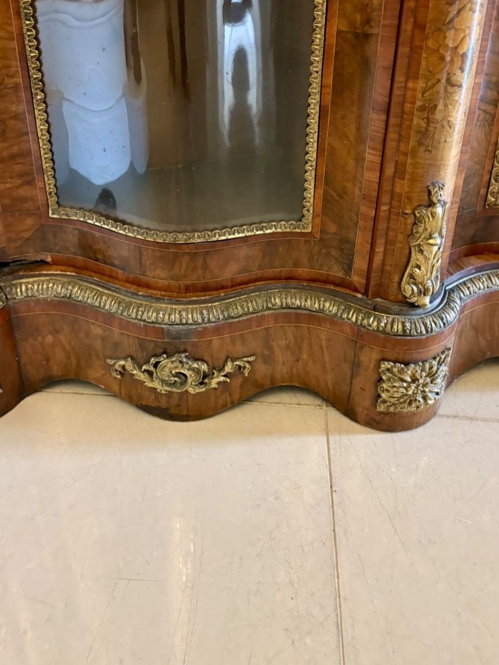 A Victorian serpentine burr walnut credenza featuring detailed floral marquetry inlays, gilt-bronze mounts, a central panelled door, and two curved glazed side doors. View VI
