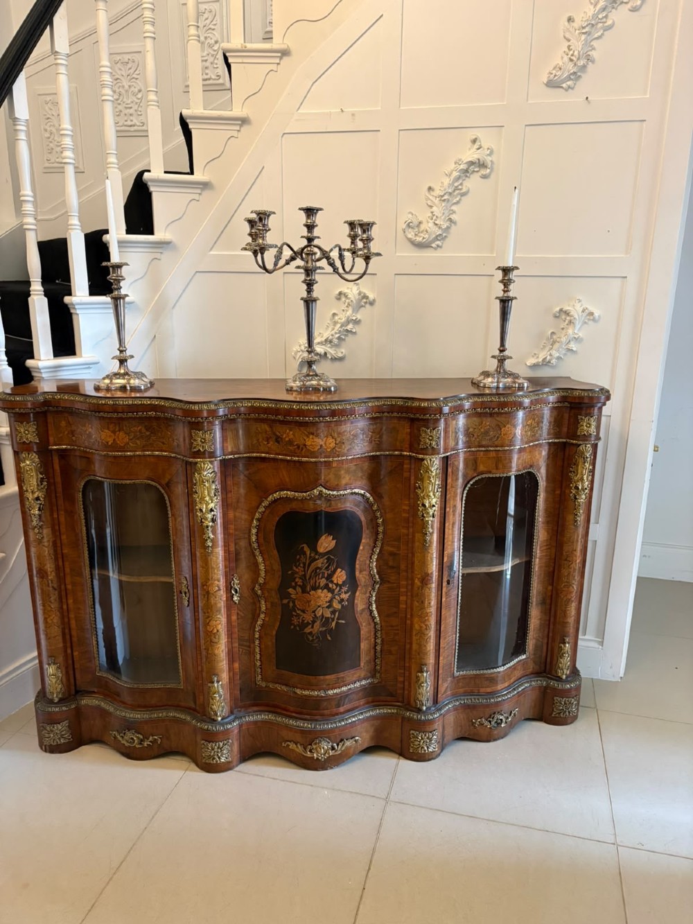 A Victorian serpentine burr walnut credenza featuring detailed floral marquetry inlays, gilt-bronze mounts, a central panelled door, and two curved glazed side doors. View VIII