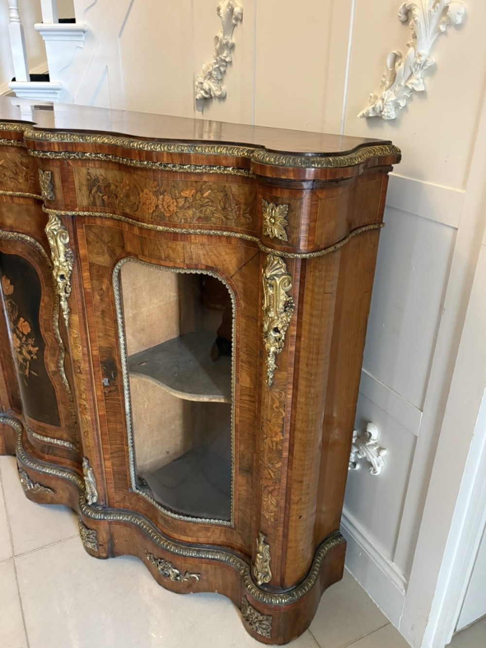 A Victorian serpentine burr walnut credenza featuring detailed floral marquetry inlays, gilt-bronze mounts, a central panelled door, and two curved glazed side doors. View XI